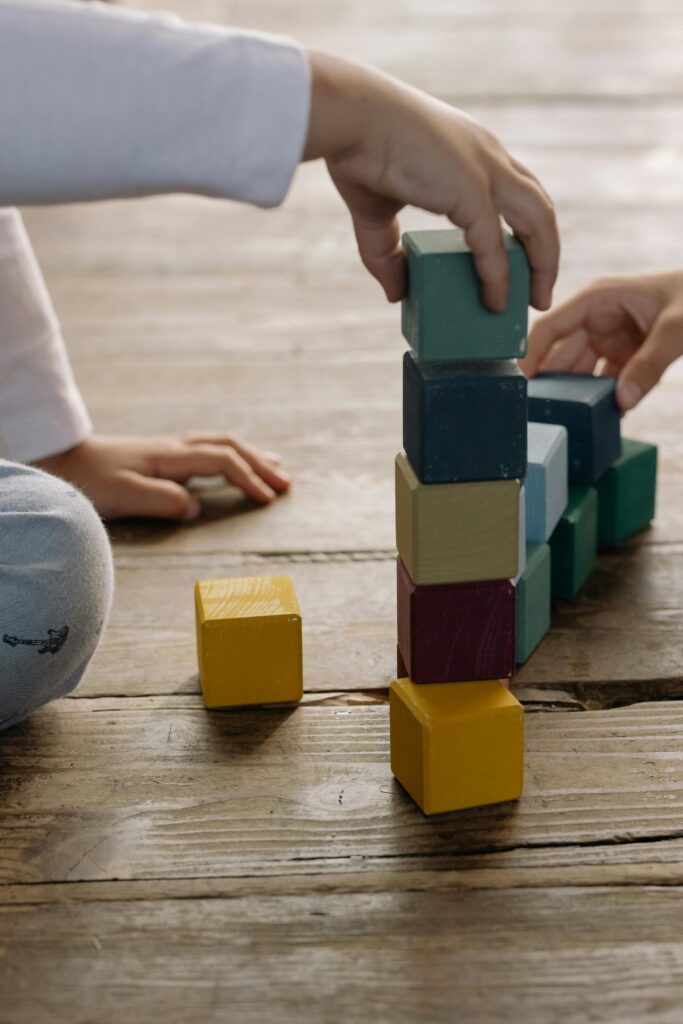Kids building a tower with colorful wooden blocks on a wooden floor indoors.